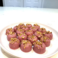Chocolate On Purpose Ruby Pistachio Truffles with layers of Pashmak (persian ferry floss) and creamy pistachio butter, dipped in pink ruby chocolate, and topped with pistachio, on a white plate. A delicious Valentine’s Day gift idea.