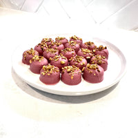 Chocolate On Purpose Ruby Pistachio Truffles with layers of Pashmak (persian ferry floss) and creamy pistachio butter, dipped in pink ruby chocolate, and topped with pistachio, on a white plate. A delicious Valentine’s Day gift idea.