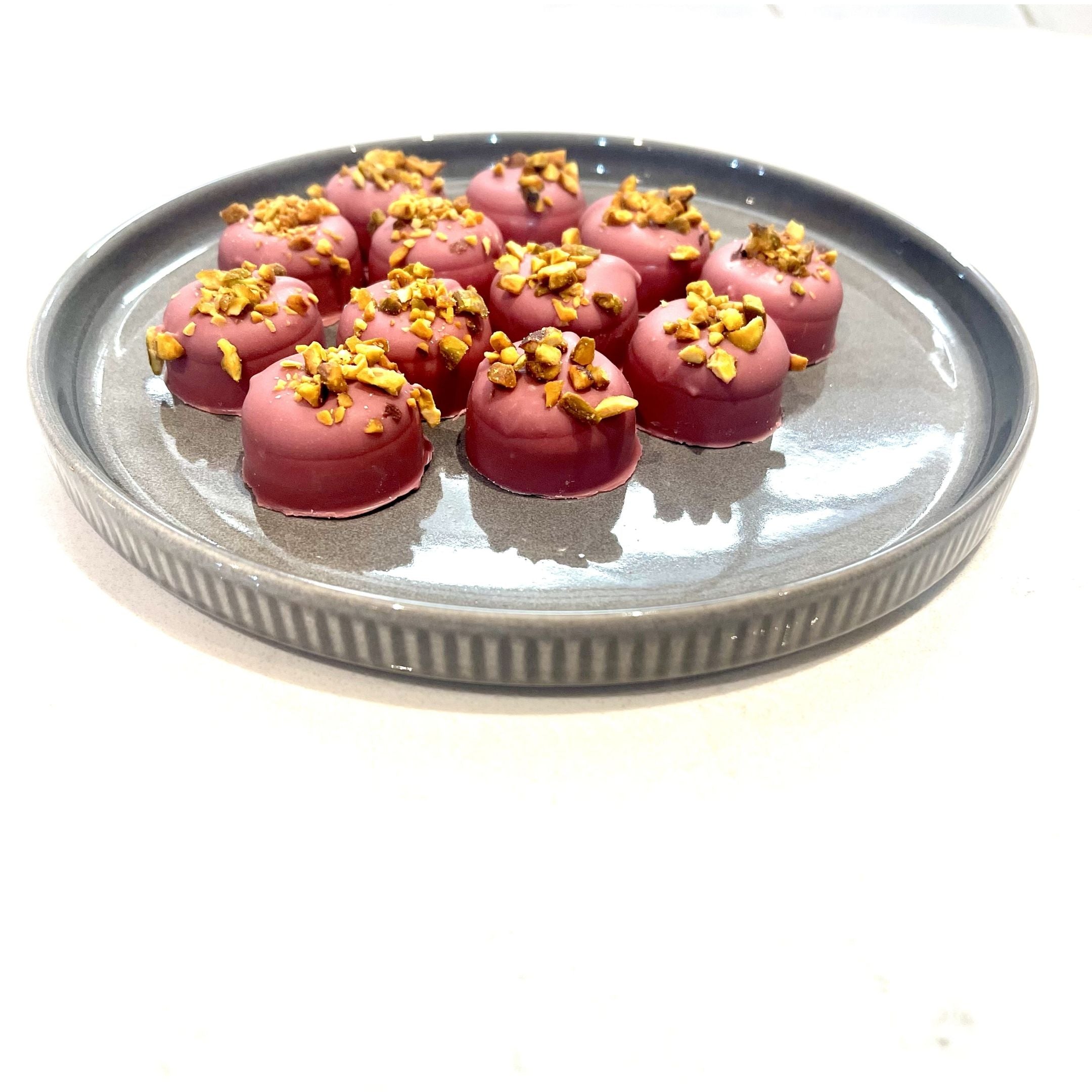 Chocolate On Purpose Ruby Pistachio Truffles with layers of Pashmak (persian ferry floss) and creamy pistachio butter, dipped in pink ruby chocolate, and topped with pistachio, on a steel blue plate. A delicious Valentine’s Day gift idea.