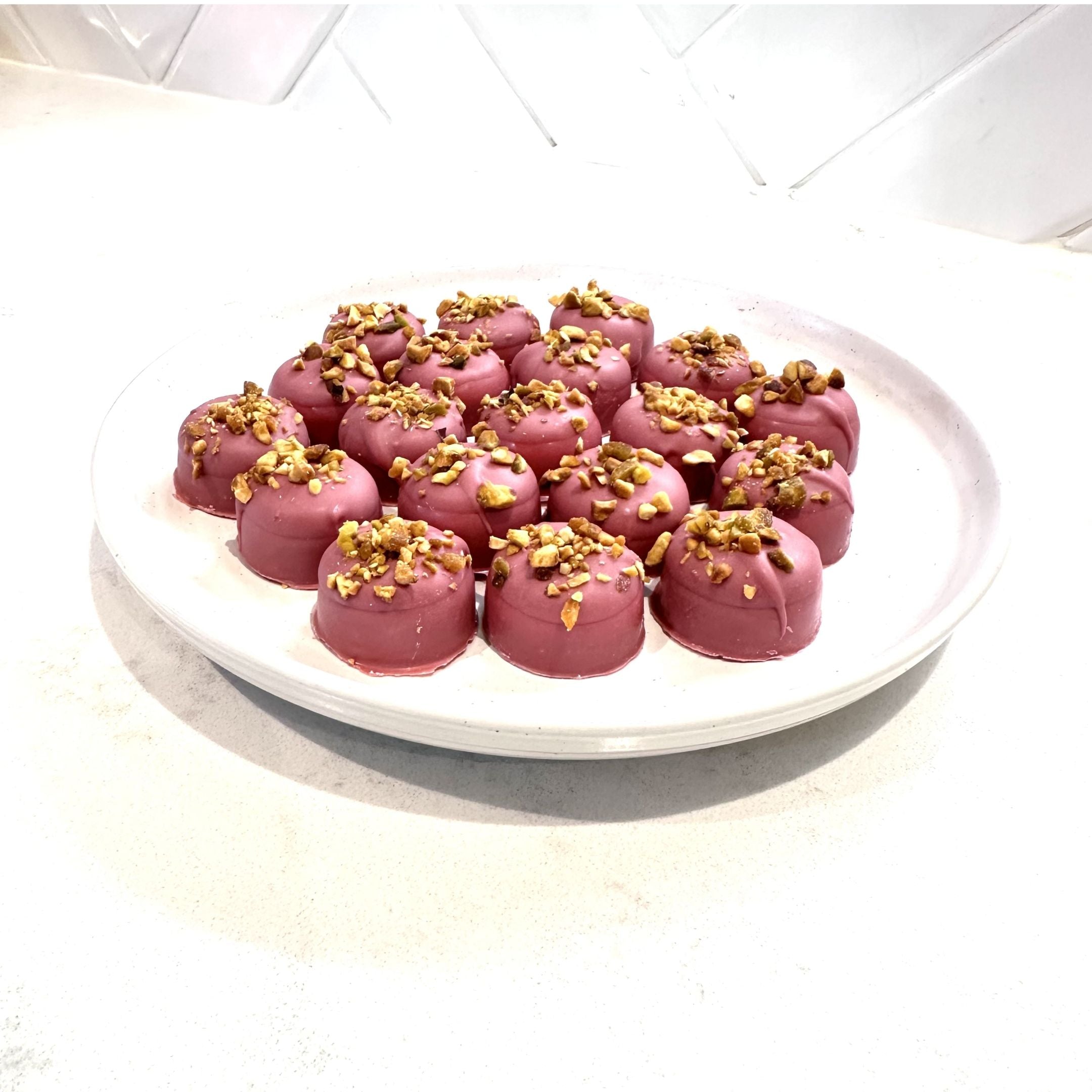 Chocolate On Purpose Ruby Pistachio Truffles with layers of Pashmak (persian ferry floss) and creamy pistachio butter, dipped in pink ruby chocolate, and topped with pistachio, on a white plate. A delicious Valentine’s Day gift idea.
