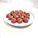 Chocolate On Purpose Ruby Pistachio Truffles with layers of Pashmak (persian ferry floss) and creamy pistachio butter, dipped in pink ruby chocolate, and topped with pistachio, on a white plate. A delicious Valentine’s Day gift idea.