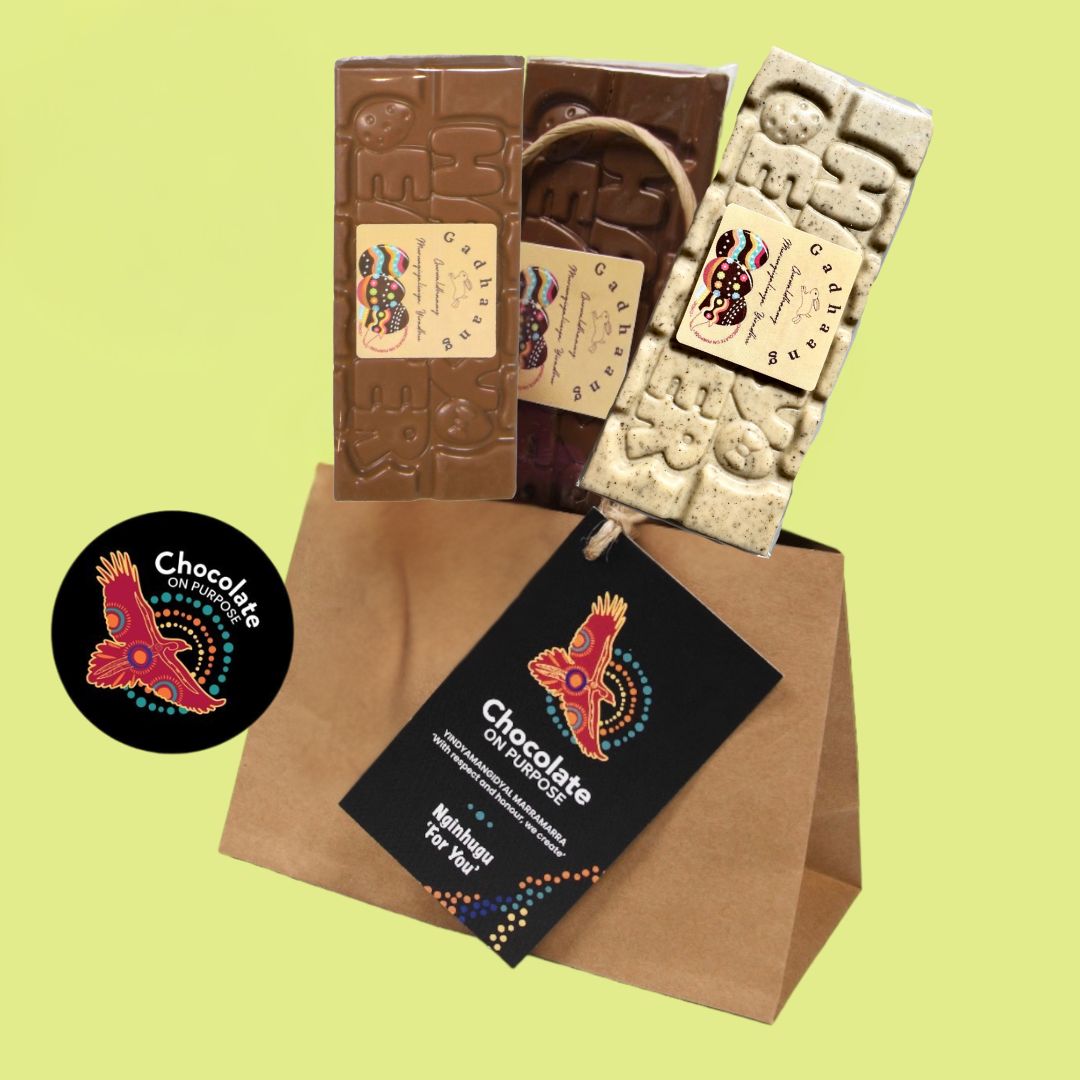 Chocolate On Purpose Easter gift bag with three 'Gadhaang Gurwaldhaany Murungiyalinya Yiradhu' “Happy Easter” Aboriginal chocolate bars in  .from left to right) Milk Chocolate with Muntrie Berry + Dark Chocolate with Davidson Plum + White Chocolate with Lemon Myrtle. Sitting in a kraft gift bag with customisable gift swing tag hanging from the handle of the bag