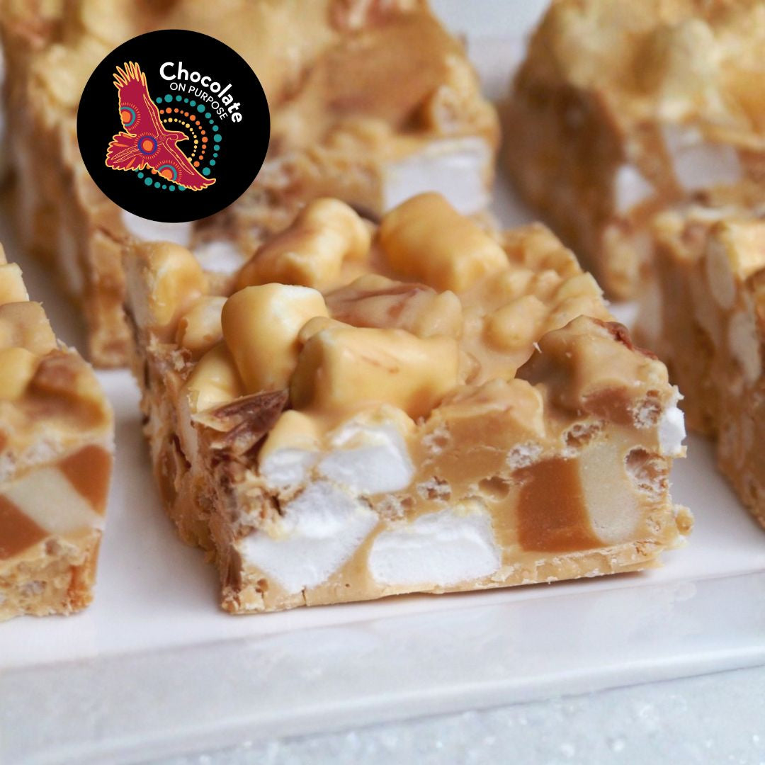 Close-up of Murru Malang golden caramelised rocky road chocolate showing marshmallows, peanuts, and sea salt flakes. Multiple pieces displayed on white surface. Chocolate On Purpose logo badge shown.