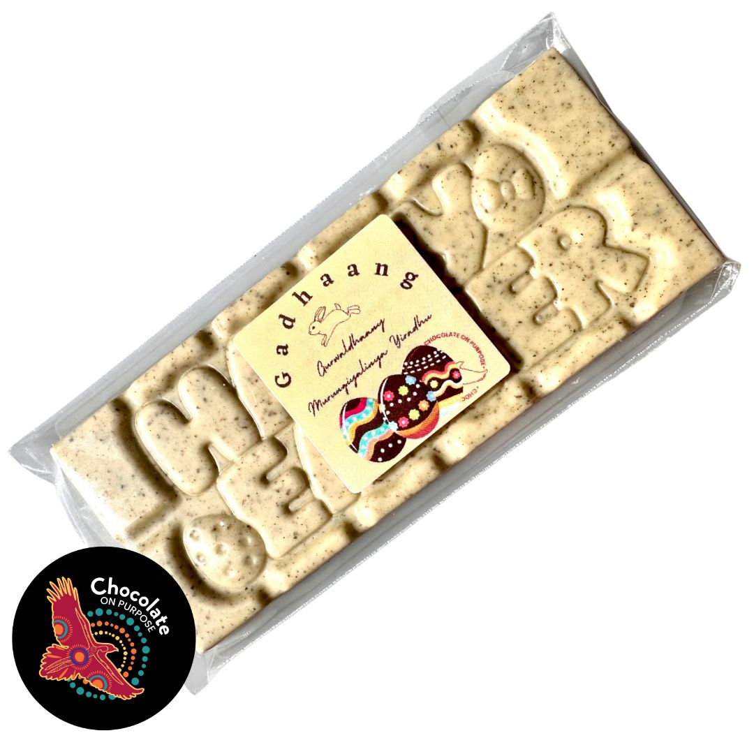 Happy Easter chocolate bar in clear wrapper, creamy white chocolate with native botanical Lemon Myrtle speckles and raised “HAPPY EASTER” lettering, with Wiradjuri Easter Greeting on Label, and Chocolate On Purpose logo on image
