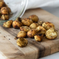 Roasted macadamias with lemon myrtle and mountain pepperberry on a wooden board. The golden nuts are lightly dusted with Girri Girri (lemon myrtle) and Mourau (mountain pepperberry), showcasing their rustic texture and vibrant seasoning. A celebration of Indigenous botanicals, artisan craft, and connection to Country by Chocolate On Purpose® — 100% Indigenous-owned, ethically sourced. Perfect for gifting or mindful snacking