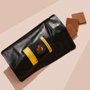 Black bag of Milk Chocoalte with Muntrie Berry (Munthari) with 3 pieces falling out. Pink beige backround 