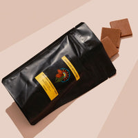 Black bag of Milk Chocoalte with Muntrie Berry (Munthari) with 3 pieces falling out. Pink beige backround 