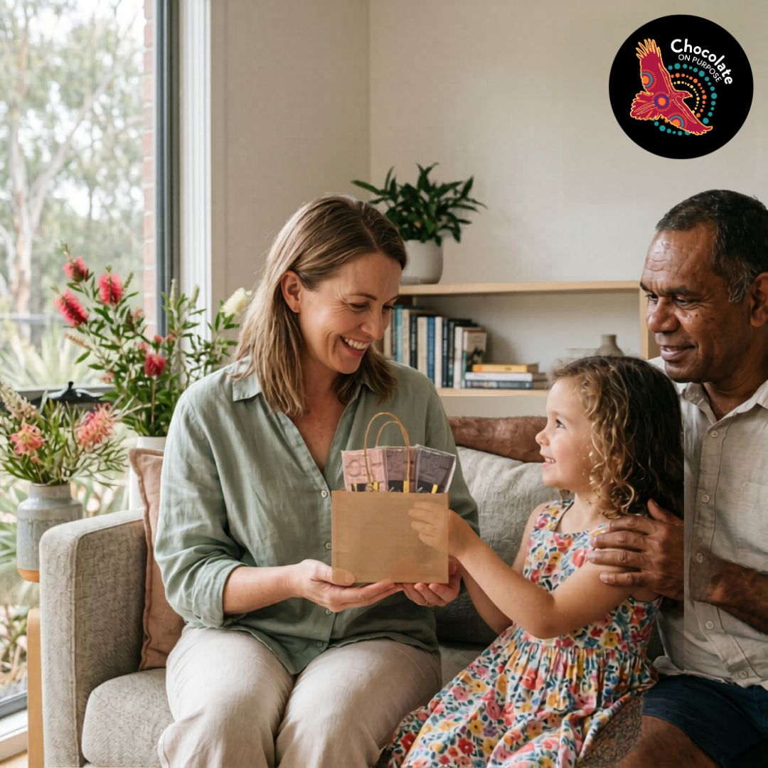 A family of mother, father, and daughther sitting on the sofa. Daughter is gifting mother with a Chocolate On Purpose Mother's Day Chocolate Gift Bag. Three Chocolate bars peep out from the top of the bag with the message 
