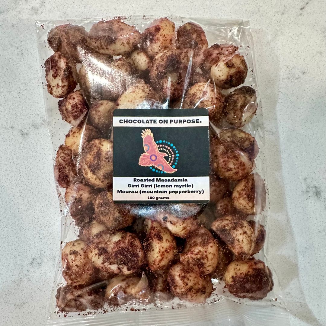 Packaged Bag of Roasted Macadamia nuts by Chocolate On Purpose®, dusted with Girri Girri (lemon myrtle) and Mourau (mountain pepperberry). The transparent packaging shows golden macadamias coated in native botanicals, with a label featuring the Chocolate On Purpose® logo and product details. Highlights Indigenous ownership, ethical sourcing, and connection to Country