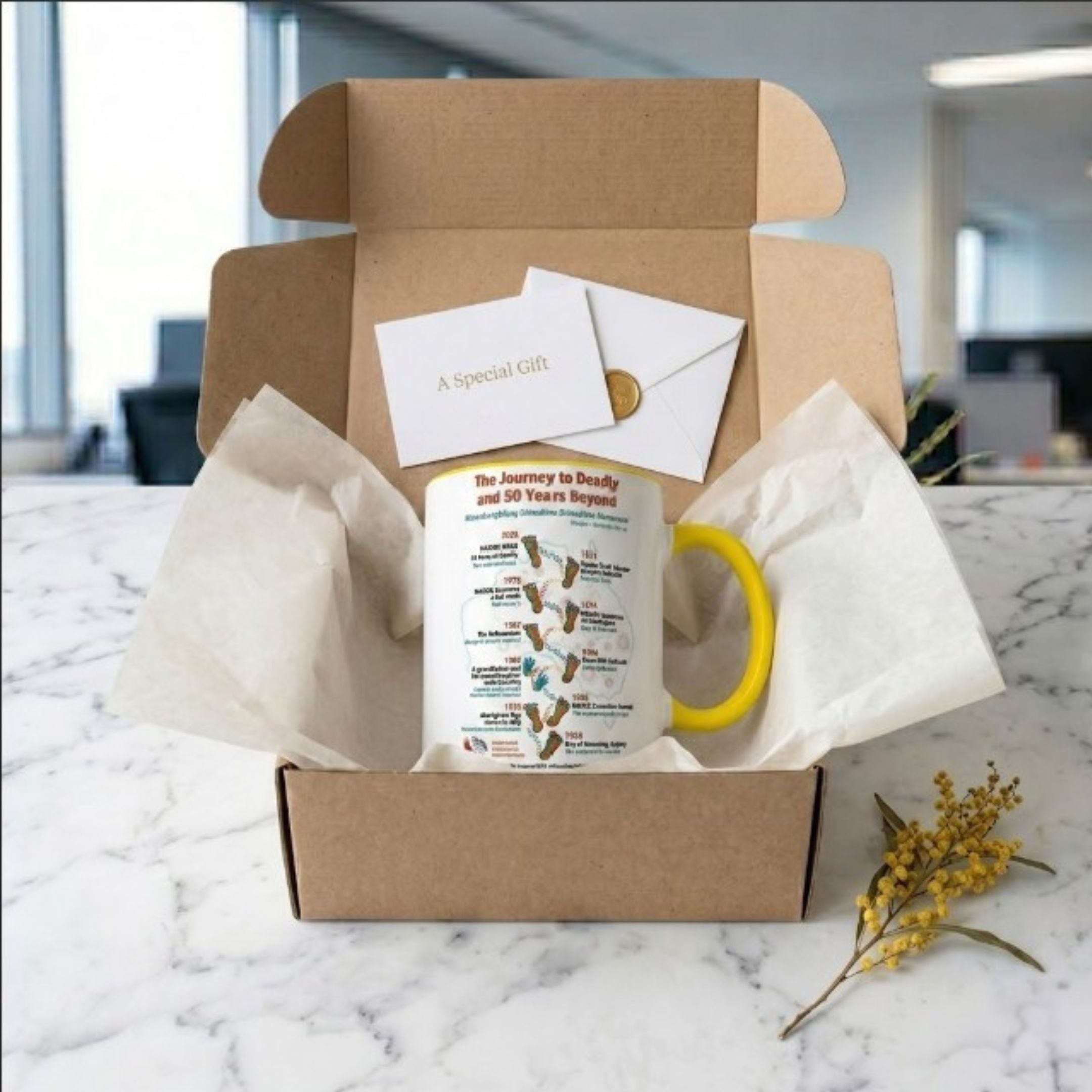 Chocolate On Purpose NAIDOC 2026 ceramic mug in open kraft gift box with tissue paper wax seal gift card and wattle sprig on marble surface