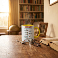 Chocolate On Purpose NAIDOC 2026 ceramic mug with yellow handle on worn timber desk beside reading glasses open book and framed photo with warm bookshelf and globe in background