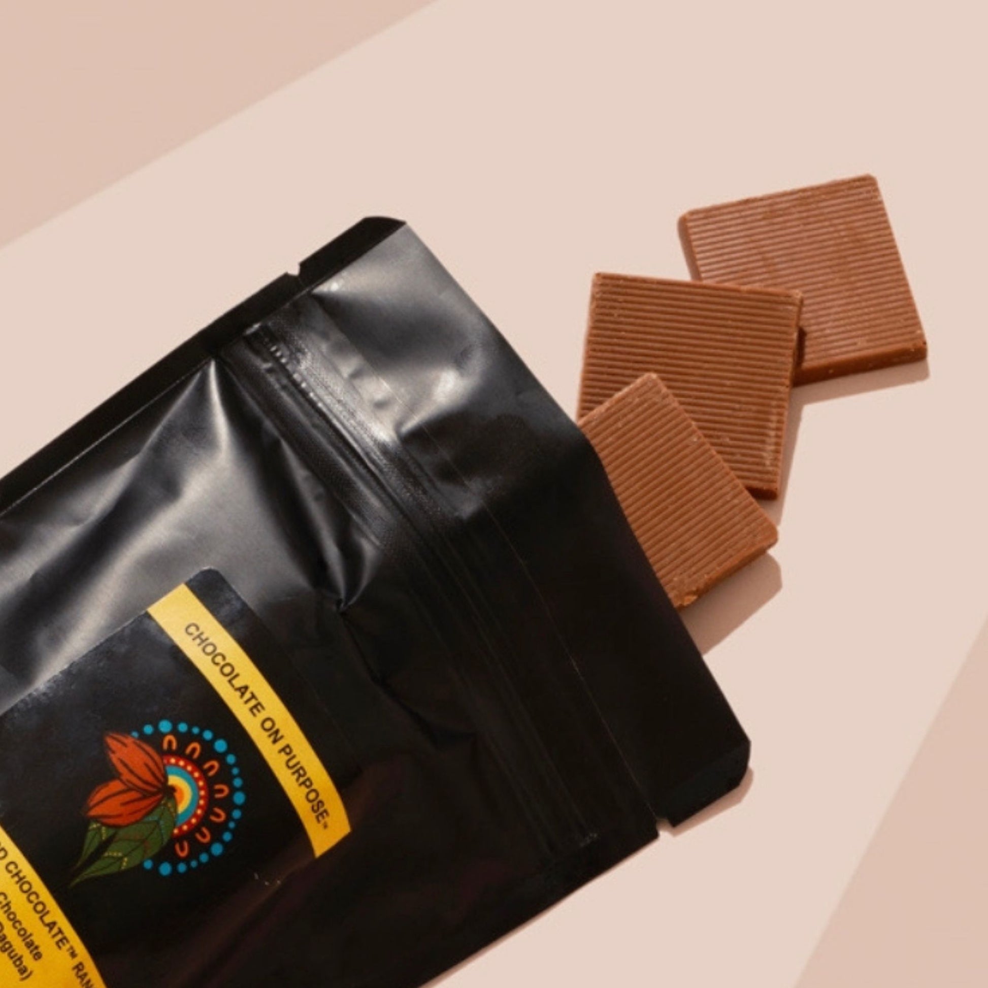 Black bag of Milk Chocoalte Riberra with 3 pieces falling out. Pink beige background 