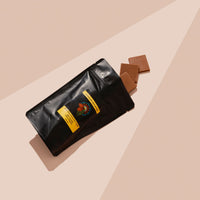 Black bag of Milk Chocoalte Riberra with 3 pieces falling out. Pink beige backround 