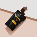 Bag of Dark Chocolate Riberra with three chocolate pieces falling out. pink and white background