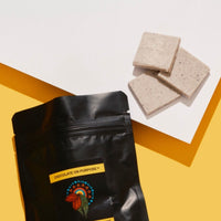 Black bag with WHITE CHOCOLATE WITH ILLAWARRA PLUM (DAALGAAL), 3 pieces of choclate next to bag. yellow and white background