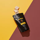 Black bag of White Chocolate with Davidson Plum 3 pieces of chocolate falling out of bag. Yellow Burgundy background